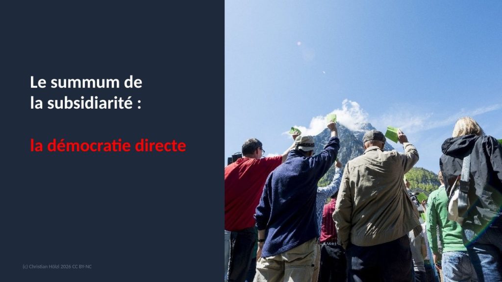 Diapositive : Le summum de la subsidiarité, la démocratie directe ; citoyens levant leur carte de vote en plein air